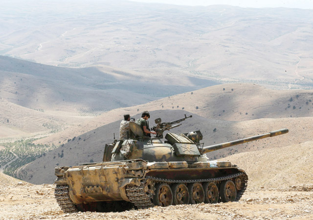 A photo taken on Wednesday during a tour guided by the Lebanese Shiite Hizbollah movement shows members of the Syrian government forces riding over a tank at a position in a mountainous area around the Syrian town of Flita near the border with Lebanon (AFP photo)