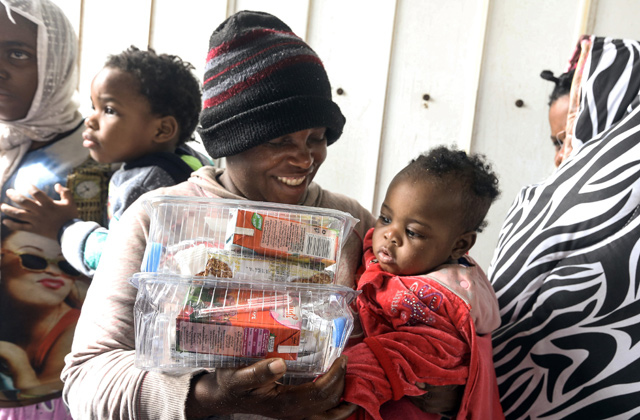 An African migrant carries a child and food packages at the dock at the Libyan capital Tripoli's naval base on Saturday, after disembarking following rescue from off the coast of Zawiyah, about 45 kilometres west of the capital (AFP photo)