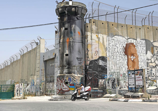 A Palestinian man rides his motorcycle past a mural painting of US President Donald Trump on Israel's controversial separation barrier in the West Bank city of Bethlehem on Monday (AFP photo)