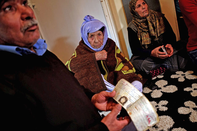 A relative shows ID papers of Laila Saleh (rear centre), a 110 years old Syrian refugee from Kobani, as she sits on the floor surrounded by members of her family, in an appartement in Athens, on December 15 (AFP photo)