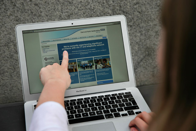 In this posed photo, a woman points to the website of the NHS: East and North Hertfordshire notifying users of a problem in its network, in London, on Friday (AFP photo)