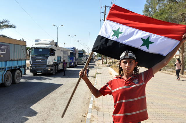 A Syrian child waves a government flag while receiving trucks carrying food aid arriving in the northeastern city of Deir Ezzor on Thursday (AFP photo)