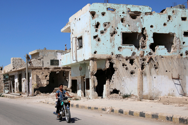 A man rides on a motorbike past damaged buildings in the rebel-held city of Inkhil, west of Daraa, Syria, on Thursday (Reuters photo)