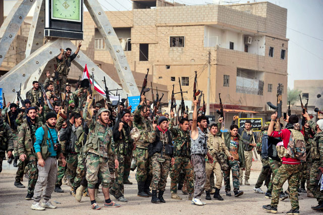This handout photo released by the official Syrian Arab News Agency  on Tuesday shows members of the pro-Syrian government forces posing with portraits of Syrian President Bashar Assad and his late father Hafez Assad while waving a national flag as they gather in a public square in the Syrian border town of Albu Kamal (AFP photo)