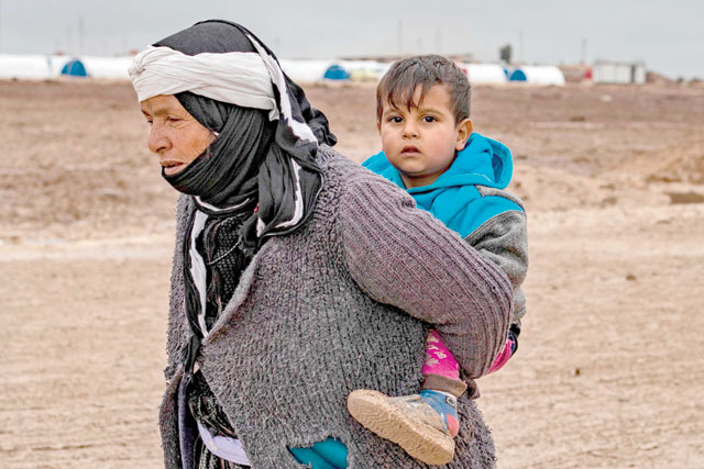 A Syrian woman walks by carrying a child on her back in the Washukanni Camp for the internally displaced, near the predominantly Kurdish city of Hasakeh in northeastern Syria, on Monday (AFP photo)