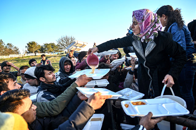 Women serve migrants food near the city of Edirne, northwestern Turkey, as they wait to cross the Meritsa River by boat and enter neighbouring Greece on Monday (AFP photo)