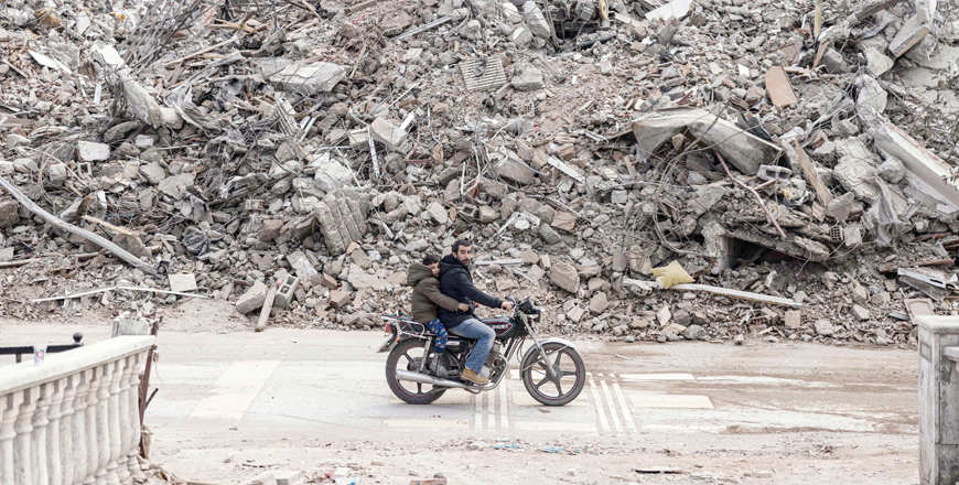 A man rides his motorcycle past collapsed buildings in the city of Antakya on Sunday (AFP photo)