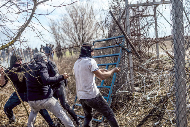 Migrants try to break fences near the Pazarkule crossing gate of the Turkey-Greece border on Saturday in the province of Edirne where makeshift camps have sprung up around the border as thousands of refugees have been encouraged by Turkey to leave for the European Union, in a bid to gain Western backing in Syria (AFP photo)