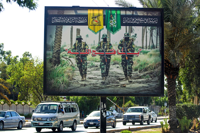 This photo taken on Wednesday shows a propaganda billboard for the pro-Iran Hizbollah Brigades militia hanging over Palestine Street in the centre of the Iraqi capital Baghdad, depicting three of their masked fighters walking along a road between palm trees (AFP  photo)