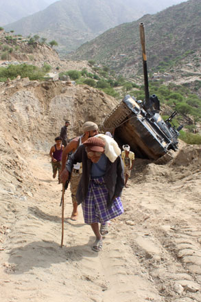 An elderly man walks past a tank belonging to the Popular Resistance Committees, supporting forces loyal to the country's exiled president, flipped on the side of the road near the village of Hifan, located southeast of the city of Taez, on Friday (AFP photo)