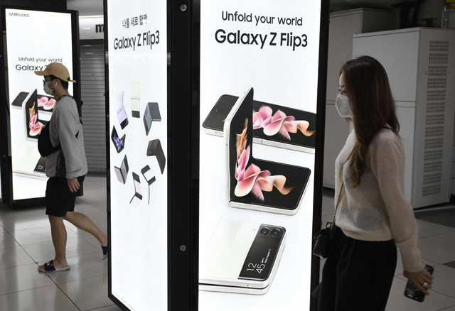 Pedestrians walk past an advertisement for the Samsung Galaxy Z Fold3 and Flip3 smartphones at an underground shopping area in Seoul, on Friday (AFP photo)