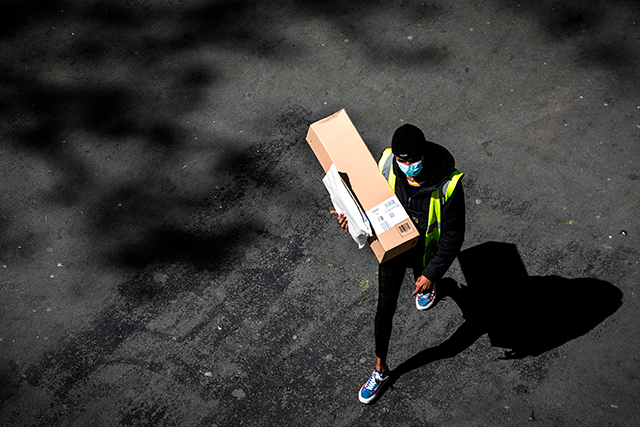 A delivery man wearing a protective mask carries an Amazon box and a letter in a street of Paris on April 15 (AFP photo) 