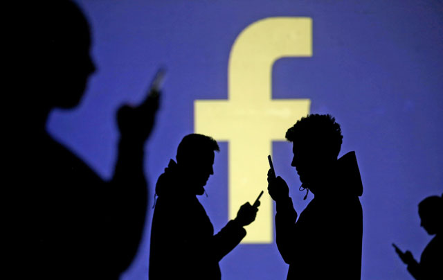 Silhouettes of mobile users are seen next to a screen projection of Facebook logo in this photo illustration taken on March 28, 2018 (Reuters file photo)