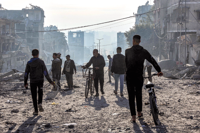 Men walk with bicycles through debris near the site of Israeli bombardment on a residential block in Jalaa Street in Gaza City on January 14, 2025 (AFP photo)