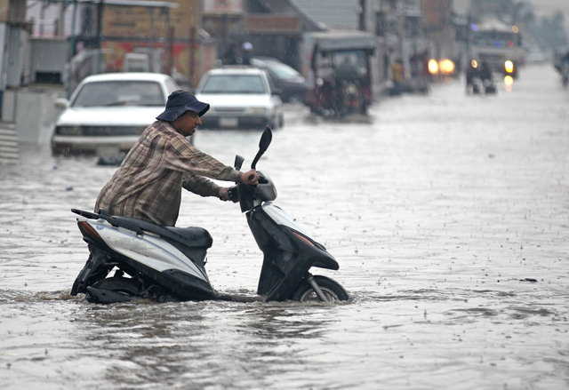 A man pushes his motorcycle through a flooded street caused by rainfall in Sadr City, east of the Baghdad, on Saturday (AFP photo)