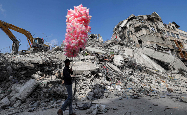 A Palestinian peddler walks with bags of cotton candy past the rubble of a building destroyed following  the May 2021 Israeli aggression on Gaza, in Gaza City's Al Rimal neighbourhood, on Thursday  (AFP photo)