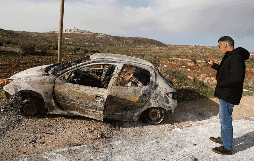 A Palestinian man photographs a charred car after it was allegedly set on fire by Israeli settlers in the village of Aqraba, east of Nablus in the occupied-West Bank, on Sunday (AFP photo)