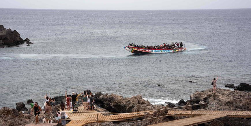 Tourists wave as African migrant people, part of a group of 242 migrants onboard of two boats, arrive onboard a 'cayuco' boat at La Restinga port on the Canary island of El Hierro on Tuesday (AFP photo)
