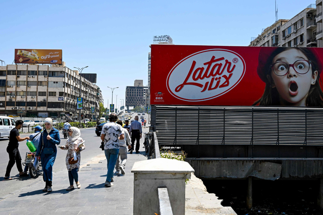 People walk past a chocolate advertisement in the Syrian capital in Damascus on Tuesday (AFP photo)