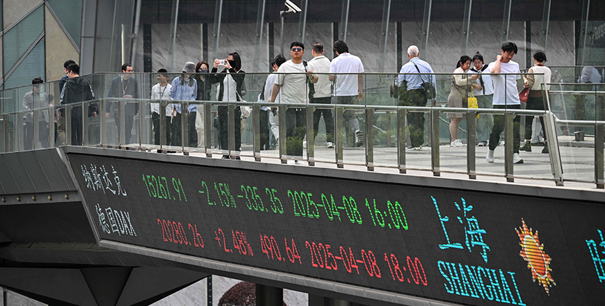People walk across a foot bridge showing a screen displaying financial markets information at the financial district in Shanghai on April 9, 2025 (AFP photo)