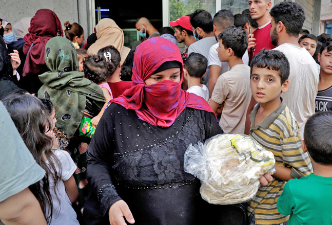 A woman leaves a bakery with a bag of bread as people wait for their turn, in the neighbourhood of Nabaa in the Lebanese capital Beirut's southern suburbs, on Friday, amidst a wave of shortages of basic items due to a severe economic crisis (AFP photo)