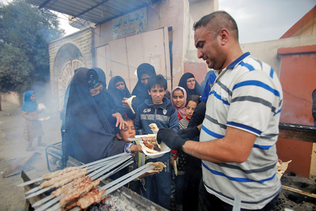 An Iraqi volunteer (right) gives food to displaced people during a battle with Daesh militants in Mosul, Iraq, on Monday (Reuters photo)