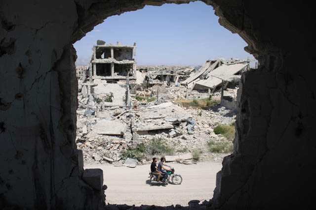 Syrians ride a motorbike past destroyed buildings in a rebel-held area of the southern city of Daraa on Wednesday (AFP photo)