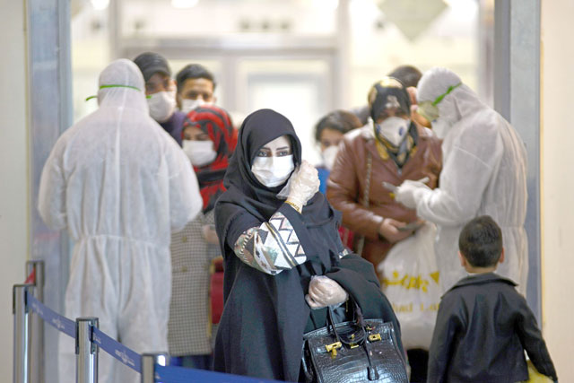 Medical staff in protective gears distribute information sheets to Iraqi passengers returning from Iran at Najaf International Airport on Thursday (AFP photo)