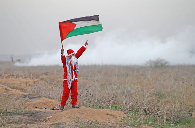 A demonstrator dressed as Santa Claus holds a Palestinian flag as Israeli troops fire tear gas during a protest against US President Donald Trump’s decision to recognise Jerusalem as the capital of Israel, near the border with Israel in the east of Gaza City, on Tuesday (Reuters photo)