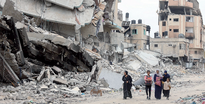 Palestinian women and children walk past the ruins of buildings destroyed by earlier Israeli bombardment in Gaza City on Monday (AFP photo)