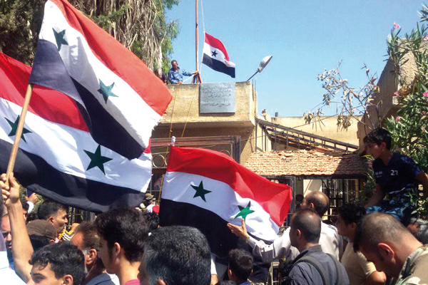 This handout photo released by the official Syrian Arab News Agency on Thursday shows Syrian men waving their national flag near the city council after Syrian regime forces took back the city of Tafas from the rebels in the Daraa countryside (AFP photo)