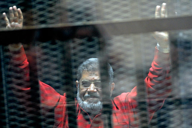 In this June 21, 2015 file photo, former Egyptian president Mohamed Morsi, wearing a red jumpsuit that designates he has been sentenced to death, raises his hands inside a defendants cage in a makeshift courtroom at the national police academy, in an eastern suburb  of Cairo, Egypt (AP photo)