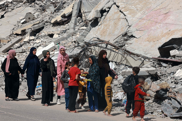 Palestinian women and children walk near a building destroyed in Israeli bombardment in Rafah in the southern Gaza Strip on Sunday, amid the ongoing Israeli war on Gaza (AFP photo)