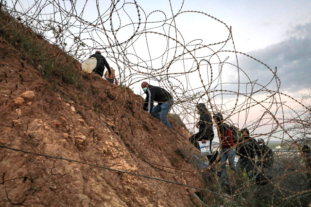 Palestinians go through a barbed-wire fence into Israel as they attempt to cross to reach their workplaces close to the Israeli checkpoint of Mitar, near Hebron in the occupied West Bank on Monday, despite a nationwide lockdown enforced by the Israeli authorities to stem a surge in COVID-19 coronavirus cases (AFP photo)