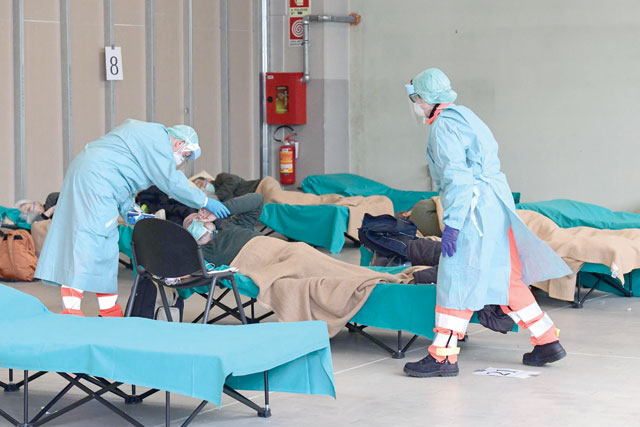 Hospital employees wearing a protection mask tend to a patient (centre) at a temporary emergency structure set up outside the accident and emergency department, where any new arrivals presenting suspect new coronavirus symptoms are being tested, at the Brescia hospital, Lombardy, on Friday (AFP photo)