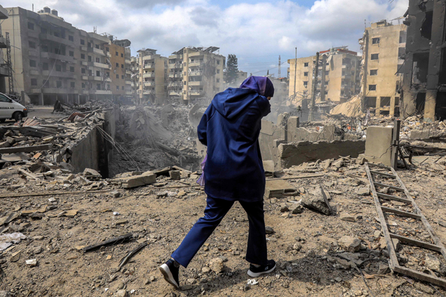 A woman walks past a crater where a collapsed building stood following an overnight Israeli air strike on the neighbourhood of Kafaat in Beirut's southern suburbs, on October 7, 2024 (AFP photo)
