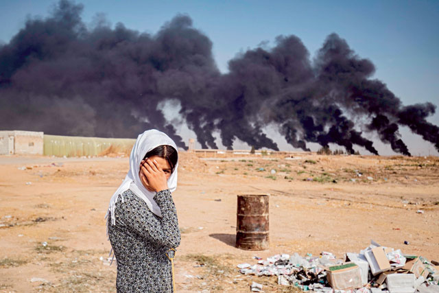 A woman covers her face as she stands along the side of a road on the outskirts of the town of Tall Tamr near the Syrian Kurdish town of Ras Al Ain along the border with Turkey in the northeastern Hasakeh province on Wednesday, with the smoke plumes of tyre fires billowing in the background to decrease visibility for Turkish warplanes that are part of operation 'Peace Spring' (AFP photo)