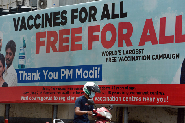 A motorist drives past a billboard advertising free COVID-19 coronavirus vaccines for all citizens near a vaccination centre in Mumbai, on Tuesday (AFP photo)