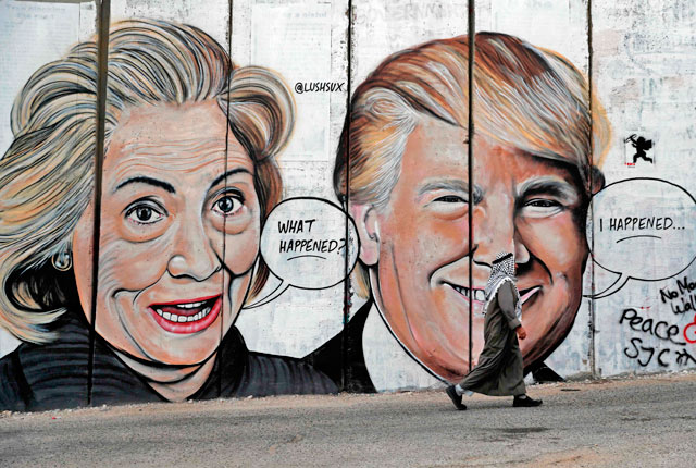 A Palestinian man walks past a newly sprayed graffiti depicting US presidential candidate Hillary Clinton and US President Donald Trump on the controversial Israeli separation wall separating the West Bank town of Bethlehem from Jerusalem on Monday (AFP photo)
