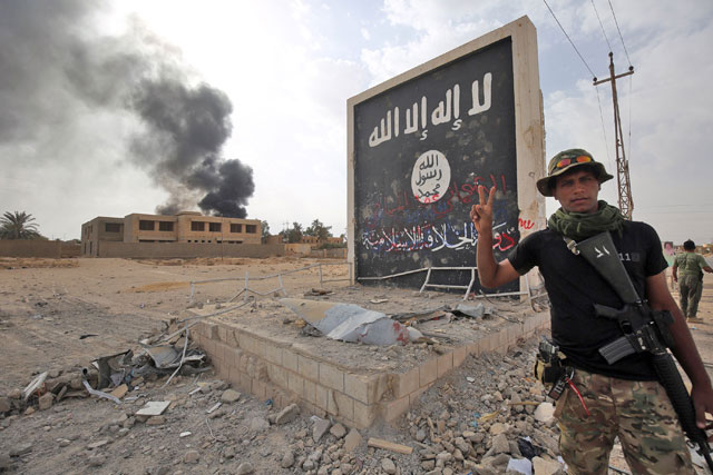Iraqi fighters of the Hashed Al Shaabi (Popular Mobilisation units) stand next to a wall bearing the Daesh group flag as they enter the city of Al Qaim, in Iraq's western Anbar province near the Syrian border, on November 3, 2017 (AFP photo)