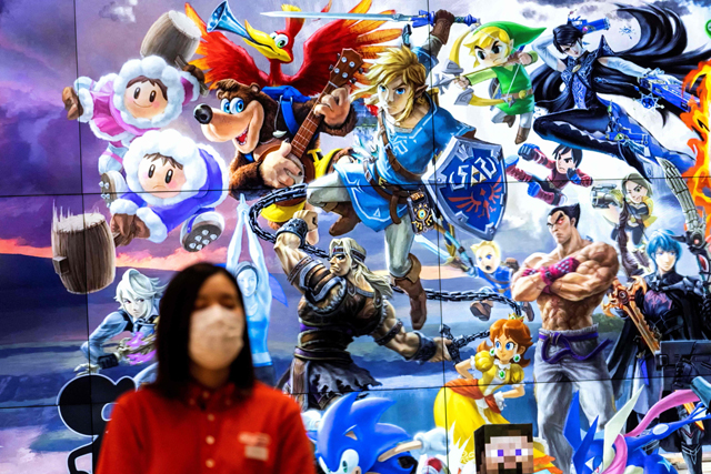 An employee wearing a face mask stands next to a screen displaying characters of different Nintendo games at a store for Japanese games giant Nintendo in Tokyo, on Thursday (AFP photo)