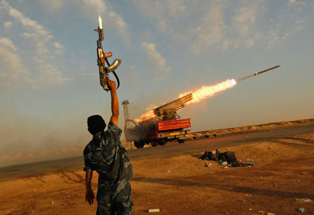 A rebel fighter celebrates as his comrades fire a rocket at troops loyal to Muammar Qaddhafi near Ajdabiyah in Libya on April 21, 2011 (File photo)