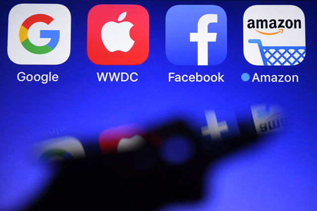 A smartphone is being operated in front of GAFA logos (acronym for Google, Apple, Facebook and Amazon web giants) as background in Hede-Bazouges, western France, on September 28, 2017 (AFP photo)