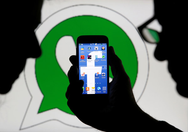 An illustration photo shows a man holding a smartphone with a Facebook logo as its screen wallpaper in front of a WhatsApp messenger logo on February 20, 2014  (Reuters file photo)