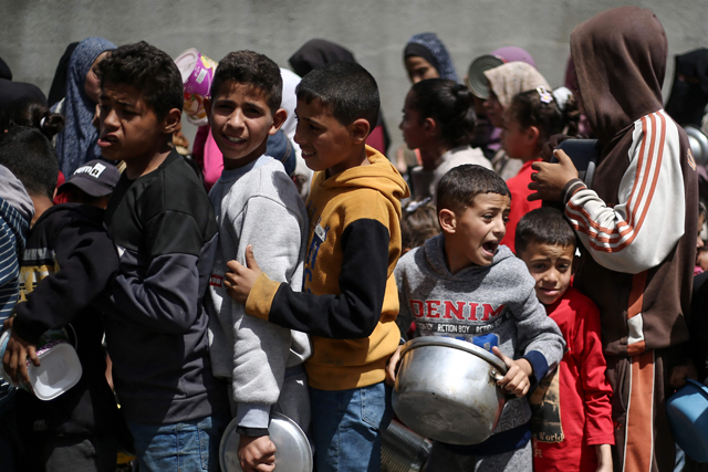 Palestinian children line up to collect a meal at a free food distribution point in the Nuseirat refugee camp in the central Gaza Strip today (AFP photo)