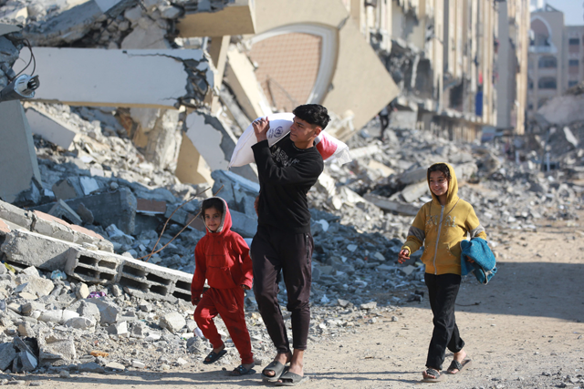 A Palestinian boy carries a bag of flour he received from an aid distrbution center in the southern Gaza Strip city of Khan Yunis on Tuesday (AFP photo)