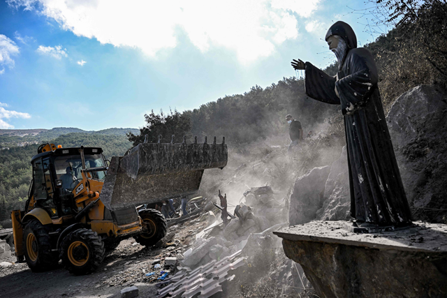 A Statue of the 19th-century Maronite Christian saint Mar Charbel is photographed as a bulldozer moves to clear rubble and debris from the site of a previous Israeli air strike on the village of Aito in northern Lebanon on Tuesday (AFP photo)