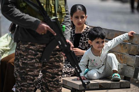 Kashmiri children sit on a bench at a marketplace as an Indian paramilitary soldier keeps guard along a street in Srinagar on May 4, 2025 (AFP photo)