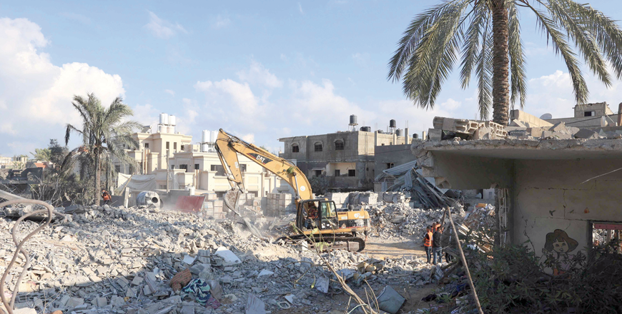 A digger moves the rubble of a destroyed building as Palestinian rescuers stand by following an Israeli airstrike in Rafah, in the southern of Gaza Strip, on Monday (AFP photo by Said Khatib)