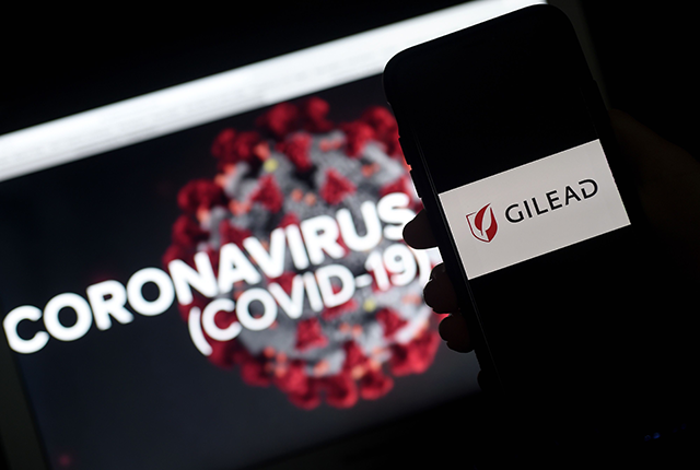 A Gilead logo is displayed on a smartphone next to a screen showing a coronavirus graphic in Arlington, Virginia on March 25, 2020 (AFP photo)